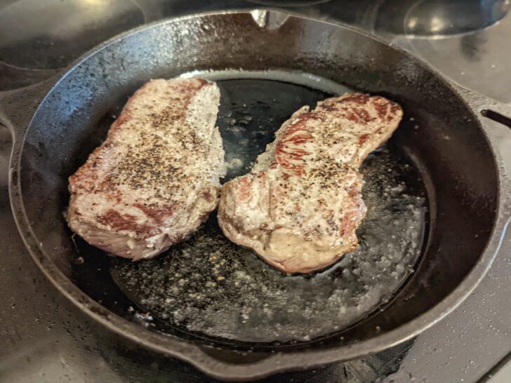 Steak cooking in a cast-iron skillet on the stovetop.