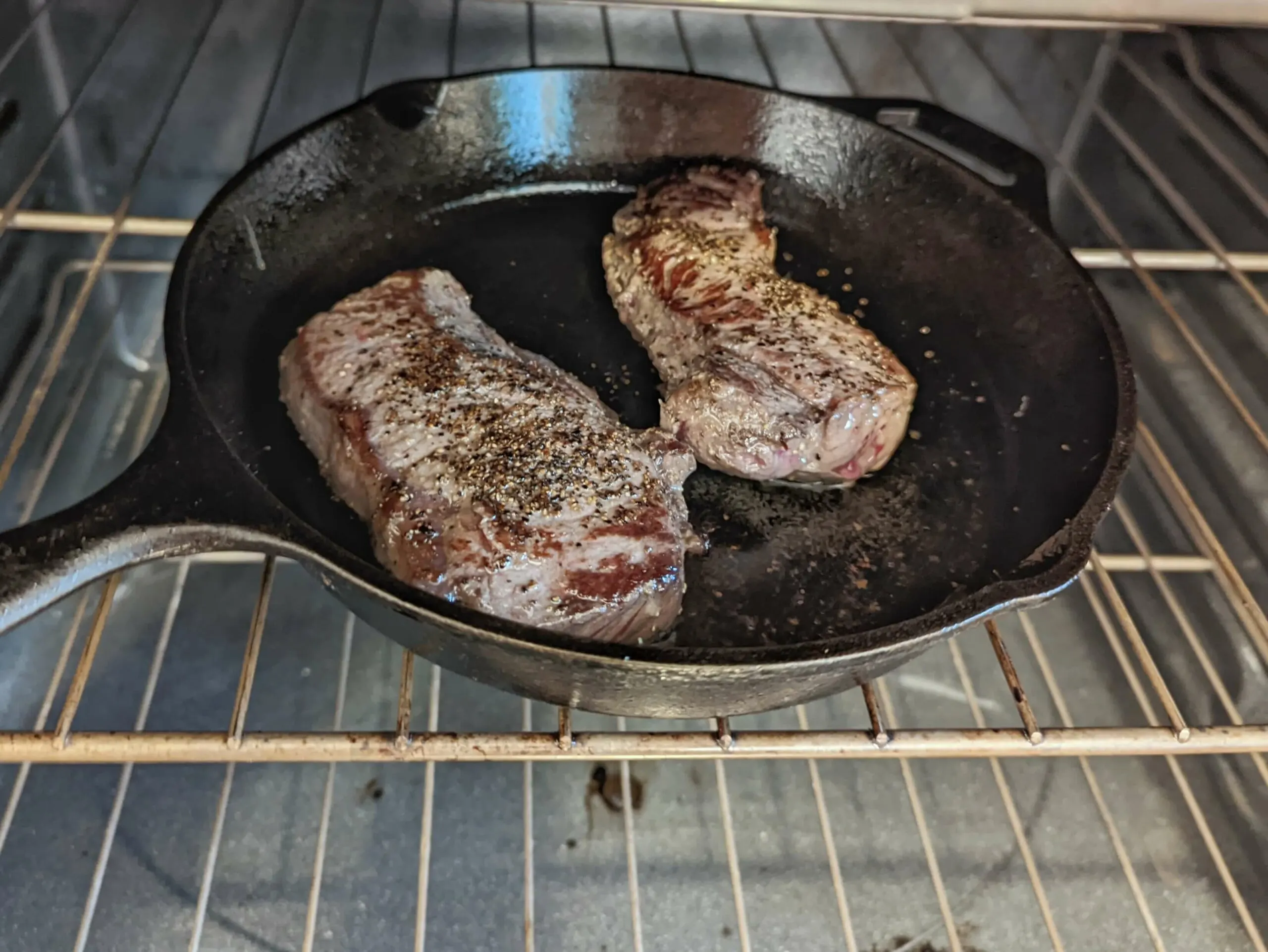 Steak cooking in a cast-iron skillet in the oven.