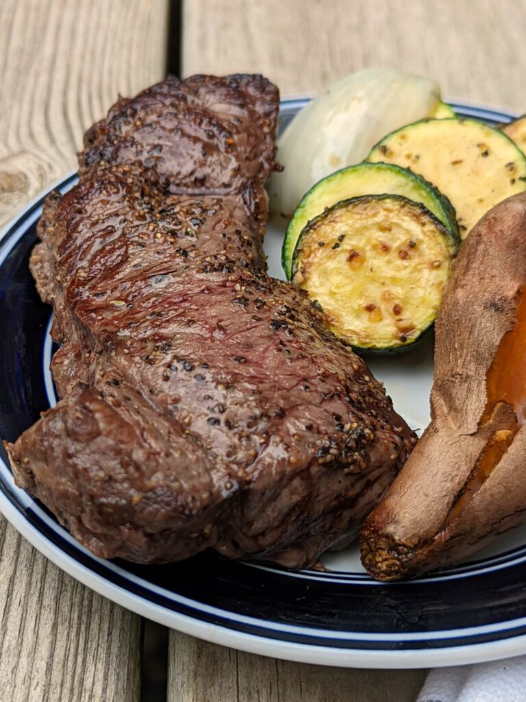 Bison steak on a plate with sweet potatoes and zucchini.
