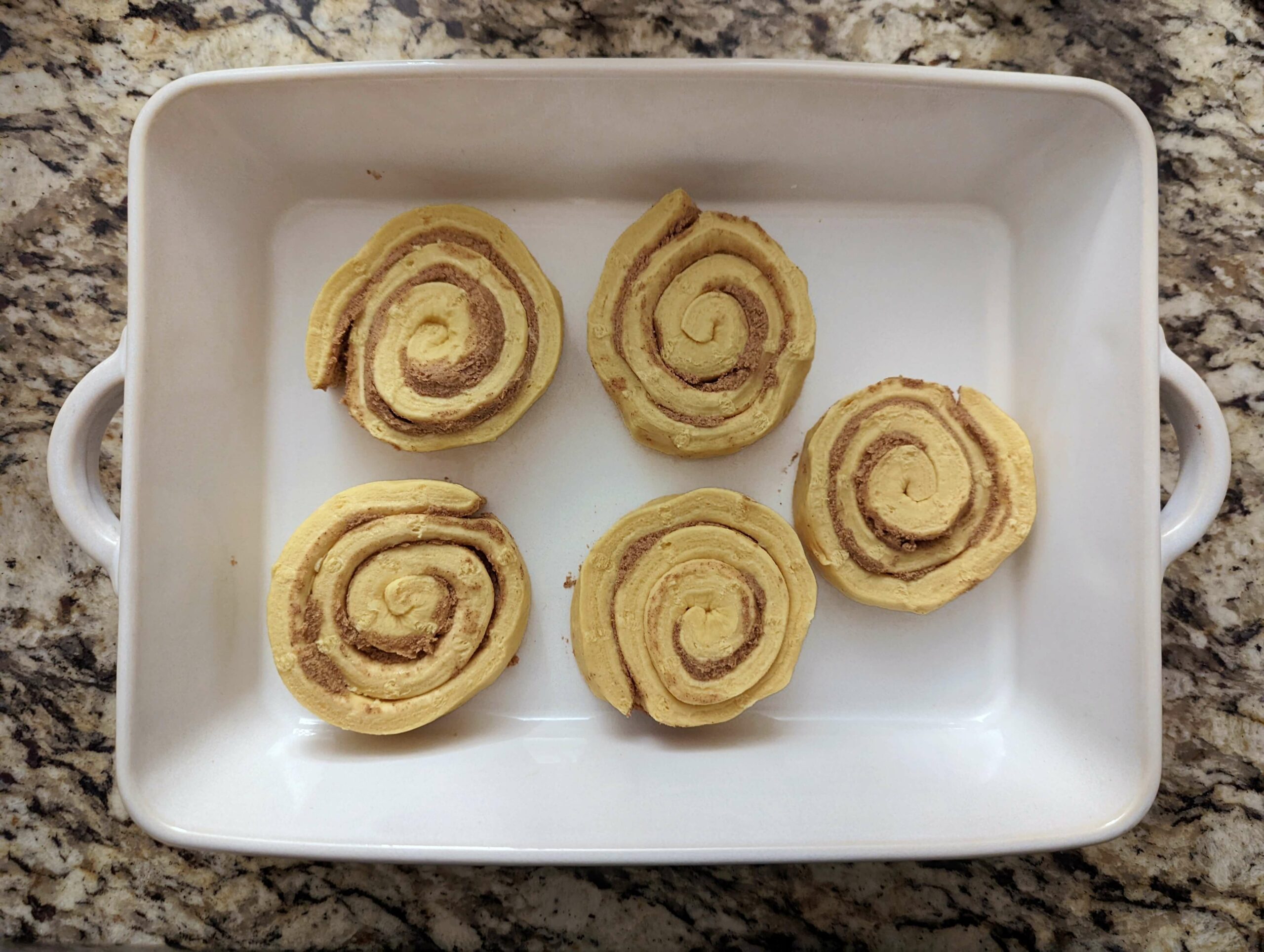 Line the cinnamon rolls into a baking pan with space to expand.