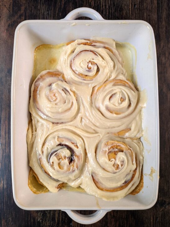 Cinnamon rolls with cream cheese frosting in a baking pan.
