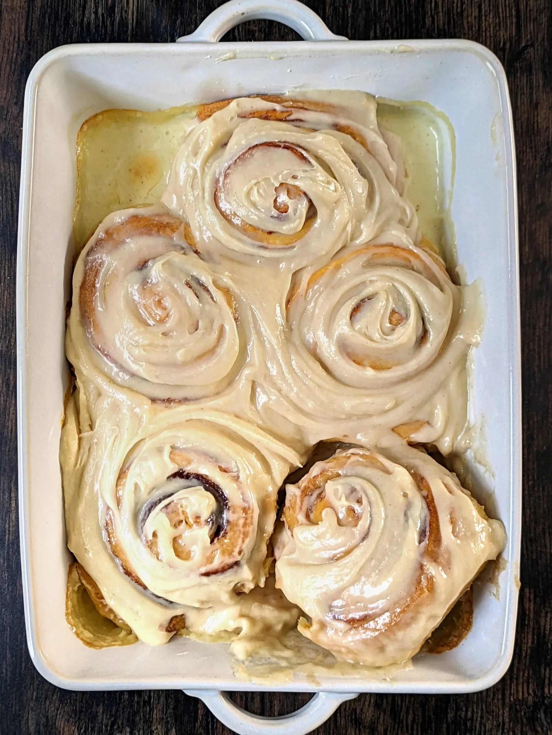 Cinnamon rolls with cream cheese frosting in a baking pan.