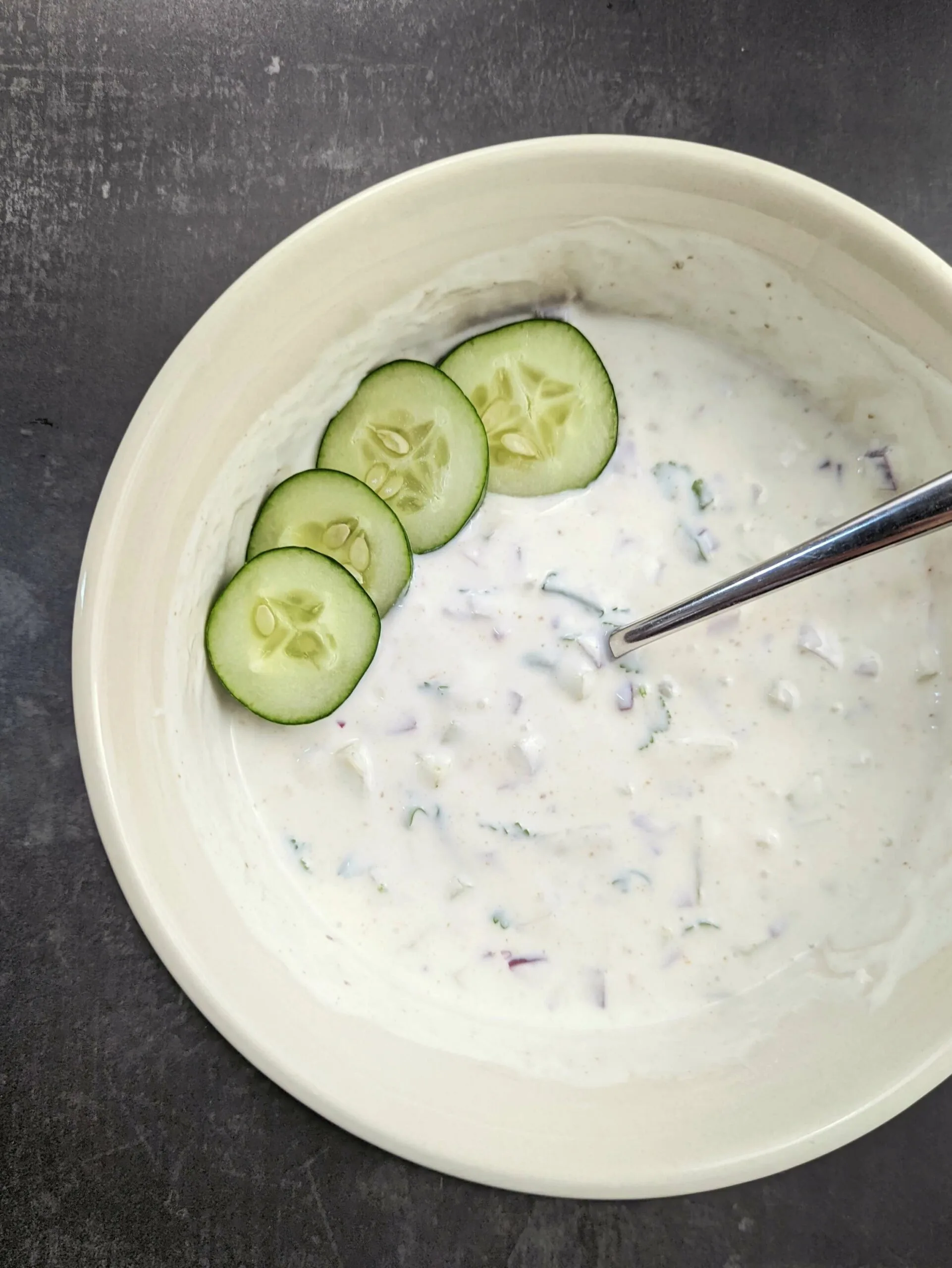 Easy raita in a bowl with cucumbers garnish.