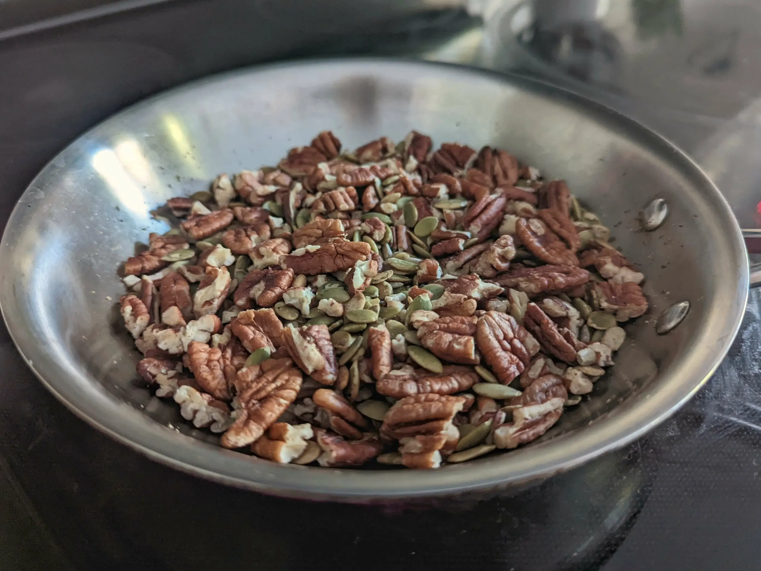 Pecans and seeds toasting in a pan.