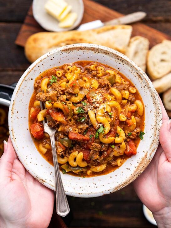 American goulash in a bowl with bread in the background.