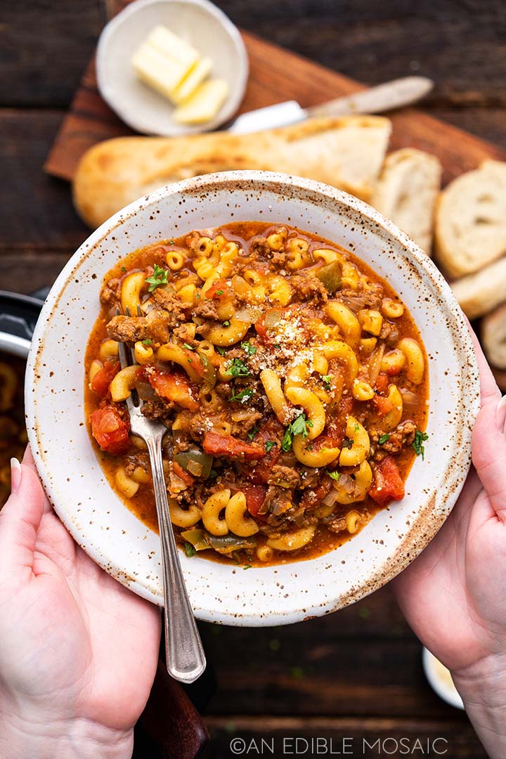 American goulash in a bowl with bread in the background.