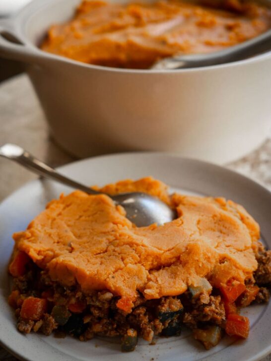 A slice of sweet potato cottage pie with the dish in the background.