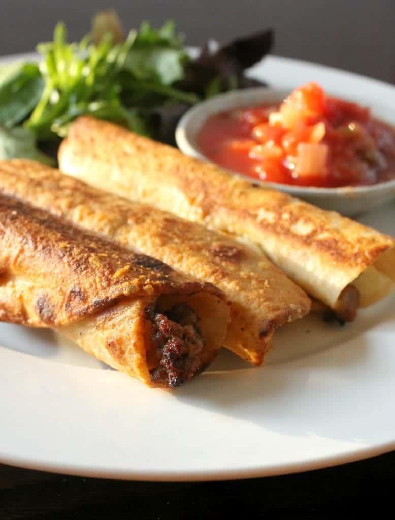 Three ground beef taquitos on a plate with salsa in the background.