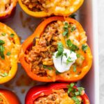 Stuffed peppers in a baking dish and topped with sour cream.