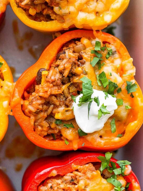 Stuffed peppers in a baking dish and topped with sour cream.