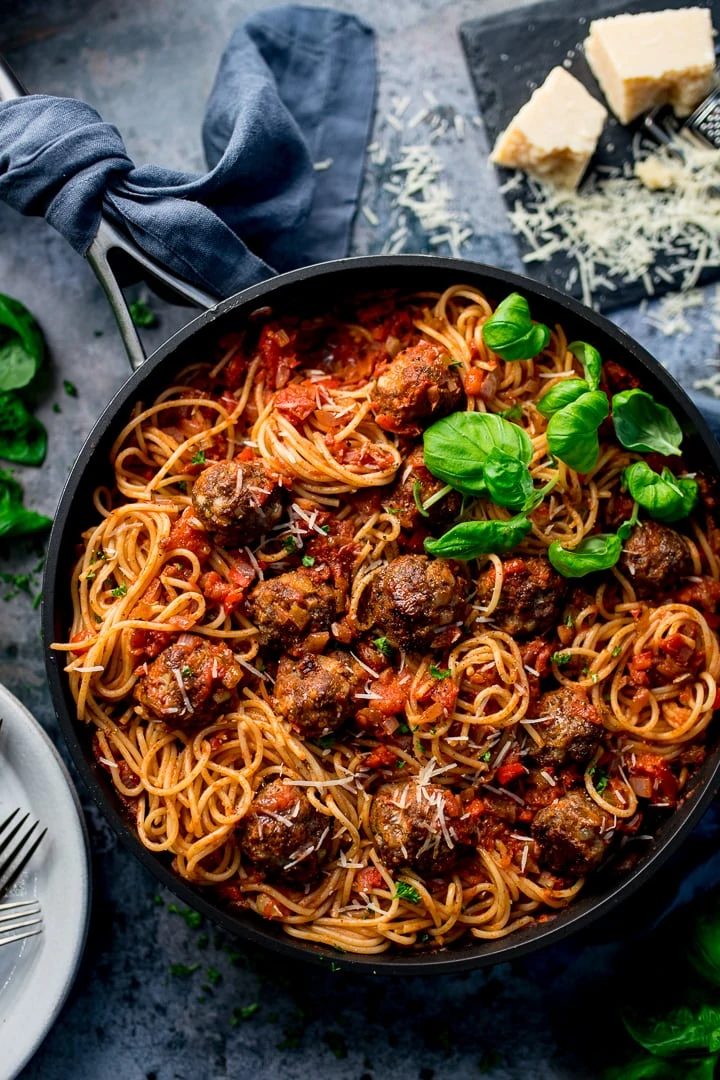 Spaghetti and meatballs in a skillet and garnished with fresh basil.