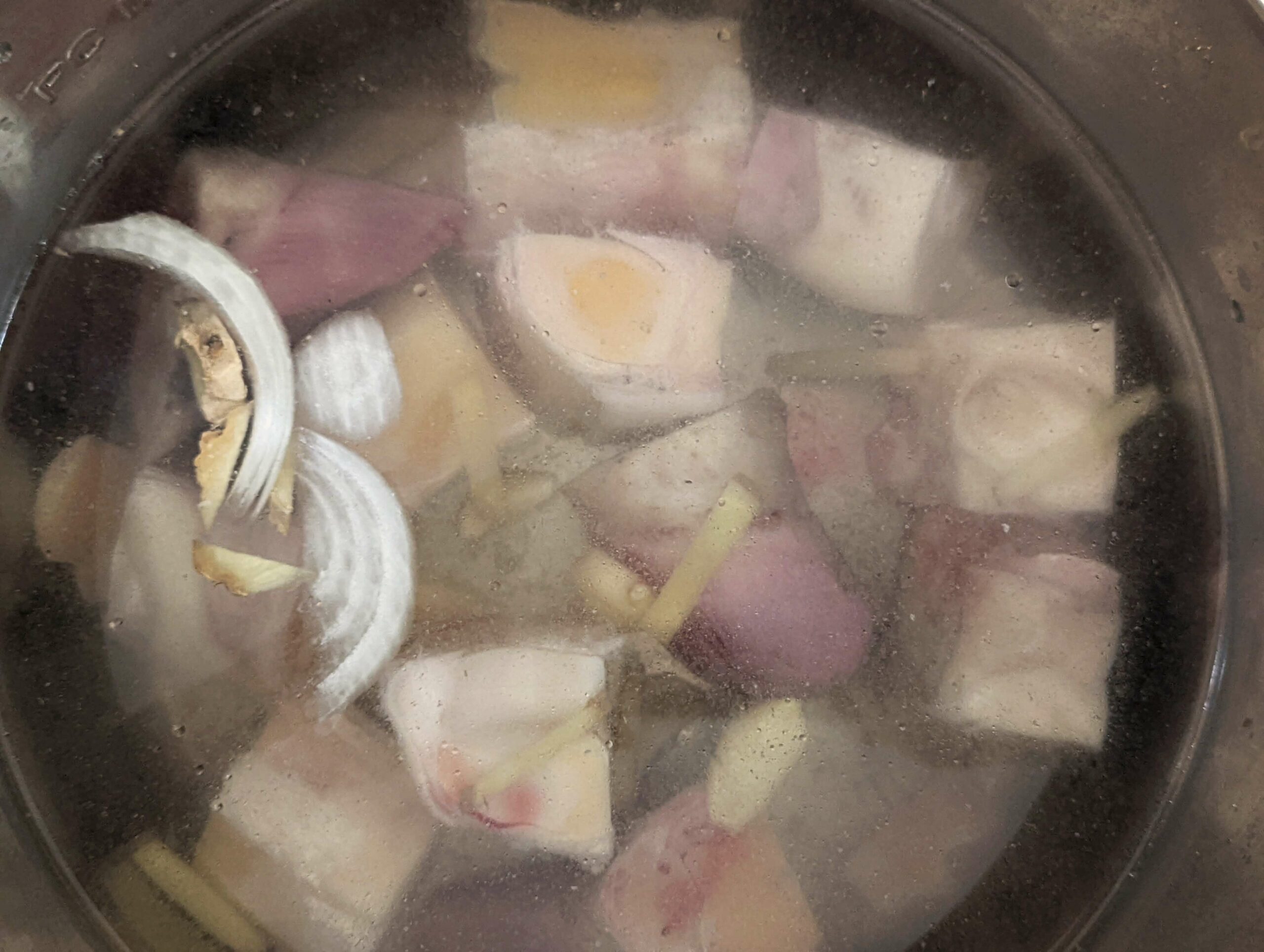 Bones, onions, garlic, ginger and herbs in a pot cooking.