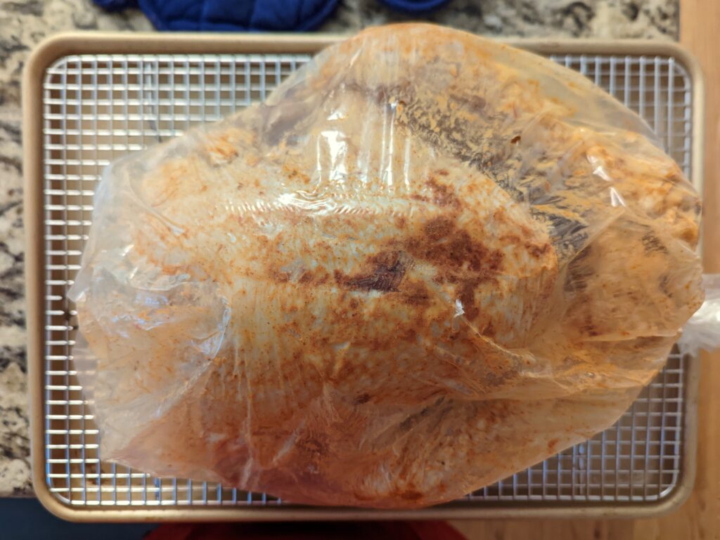 The turkey stuffed into a turkey bag on a baking rack.