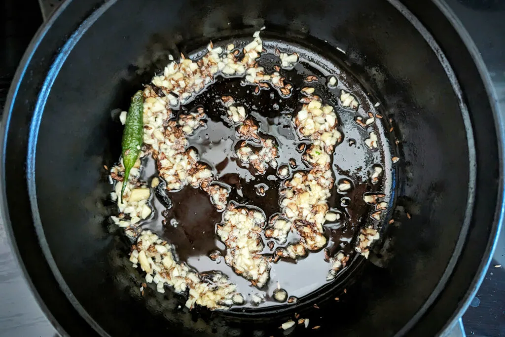 Garlic, ginger, green chilies, and whole spices in a pan.