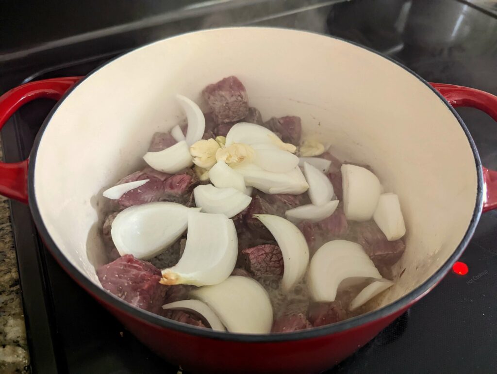 Brisket, onion, and garlic cooking in a Dutch oven.