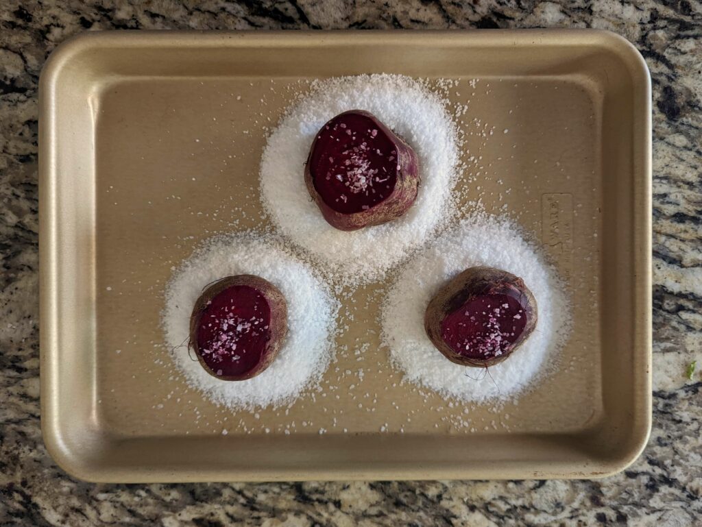 Beets on a rimmed baking dish surrounded by salt to salt roast.