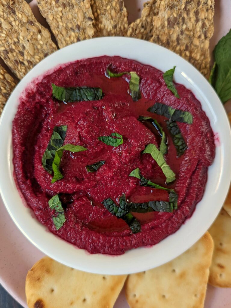 Beetroot dip surrounded by crackers and naan bites.