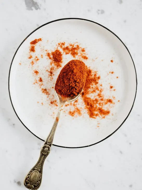 Paprika on a spoon with it spilled on the surface.