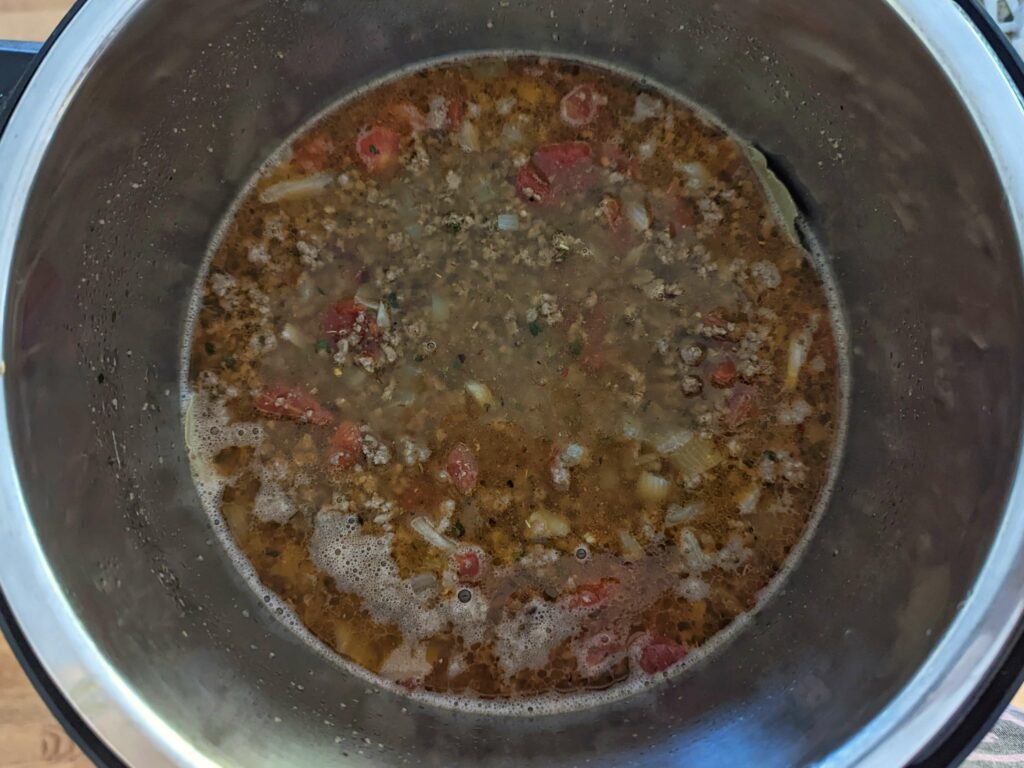Chicken broth and bay leaves in an Instant Pot along with Italian sausage, tomatoes, onion, and garlic.
