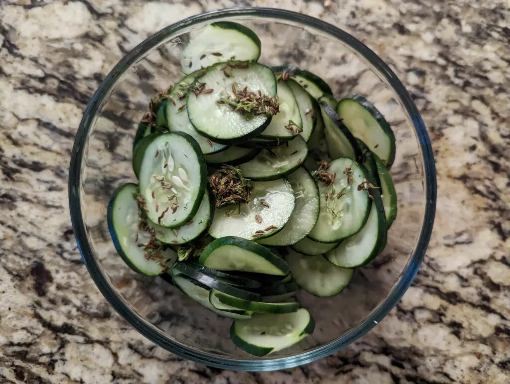 Vinegar mixture poured over the cucumbers in a glass bowl.