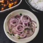 A bowl of onion salad with a plate of rice and chicken in the background.