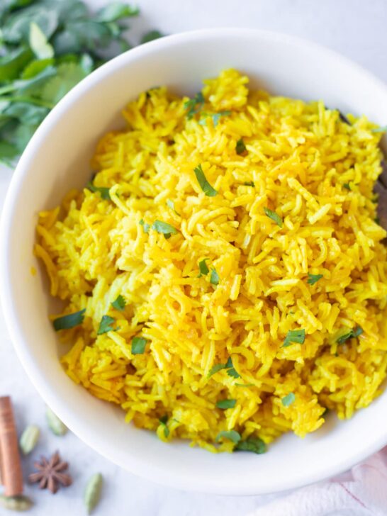 A bowl of turmeric yellow rice with cilantro in the background.