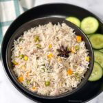 Vegetable pulao in a bowl with cucumber slices on the side.