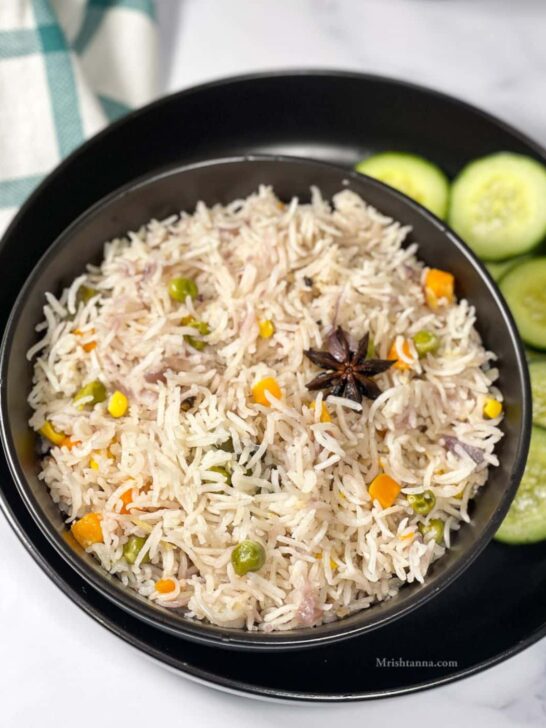 Vegetable pulao in a bowl with cucumber slices on the side.