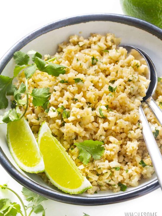 Coconut cauliflower rice topped with cilantro and lime wedges.