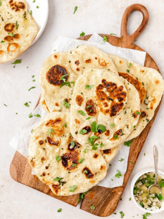 Naan on a table garnished with garlic butter and cilantro. 