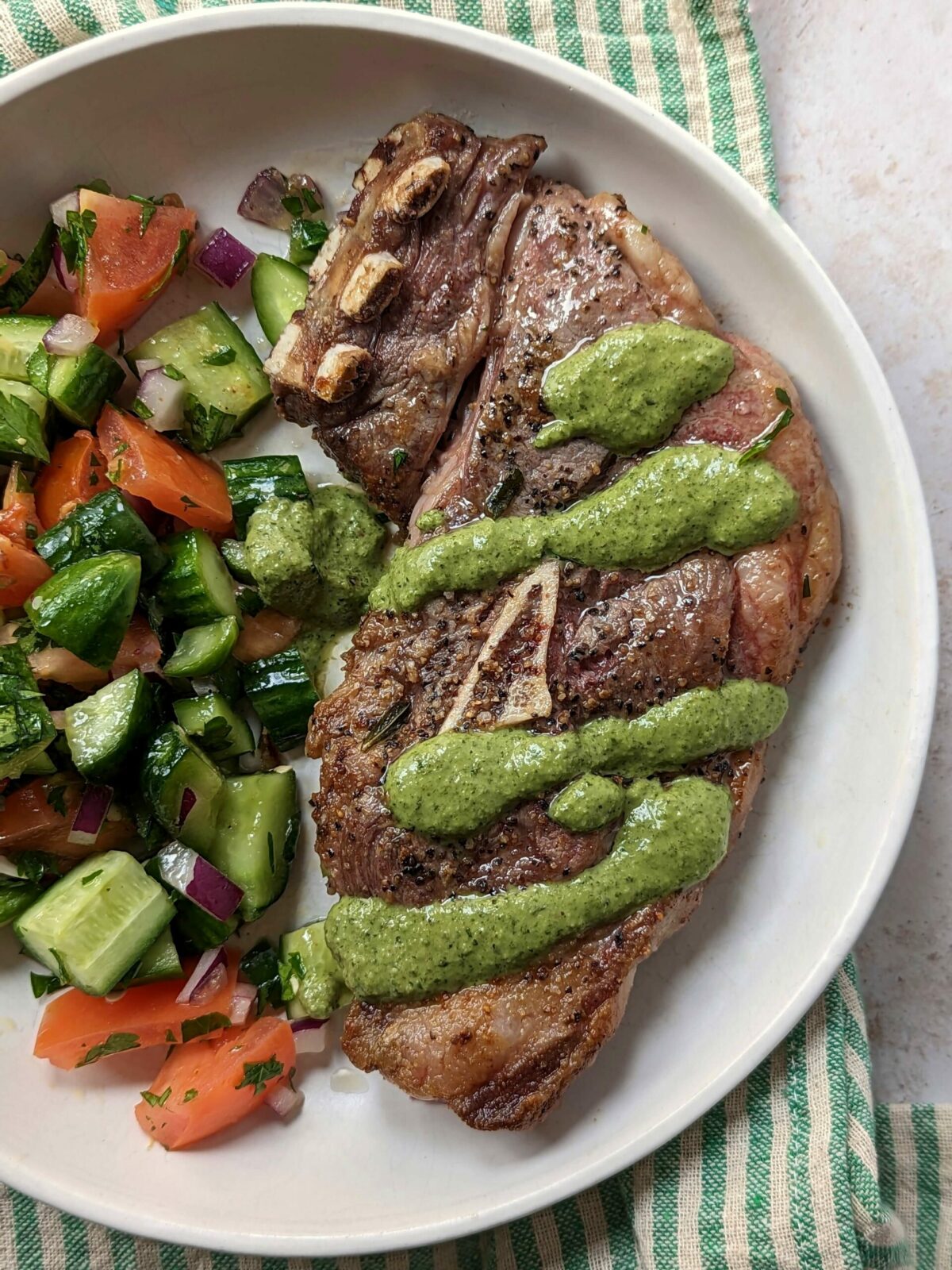Lamb shoulder chop served with cucumber and tomato salad and topped with mint chutney.