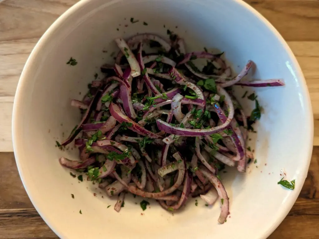 Olive oil, lemon juice, sumac, parsley, and onions in a bowl. 