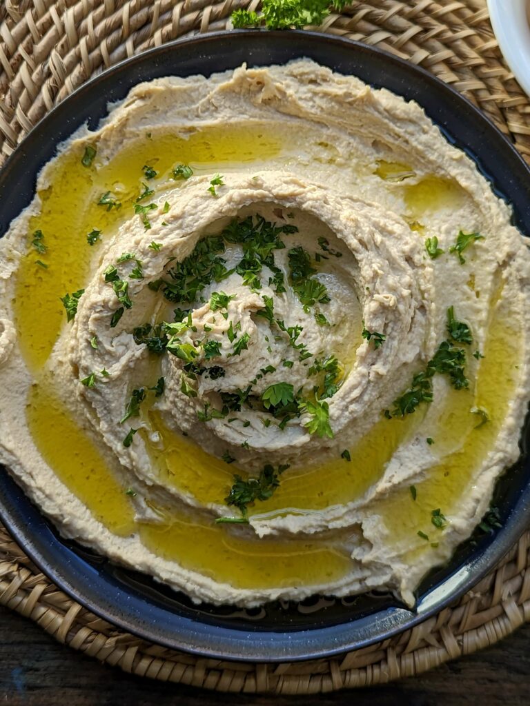 Hummus on a plate garnished with olive oil and parsley.