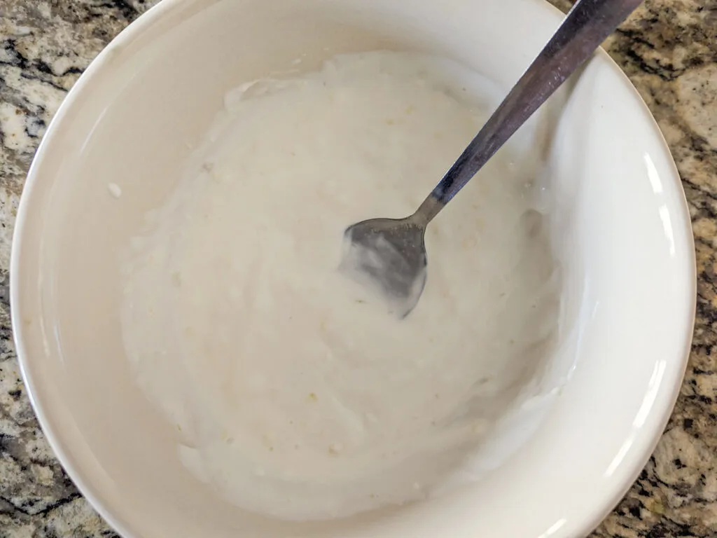 Yogurt mixed with garlic in a small bowl with a spoon in it.