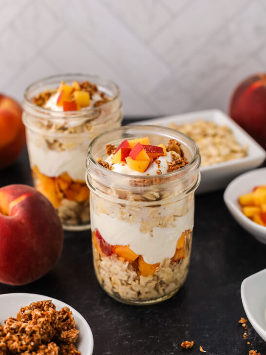 A picture of two containers of peach overnight oats with peaches in the background. 