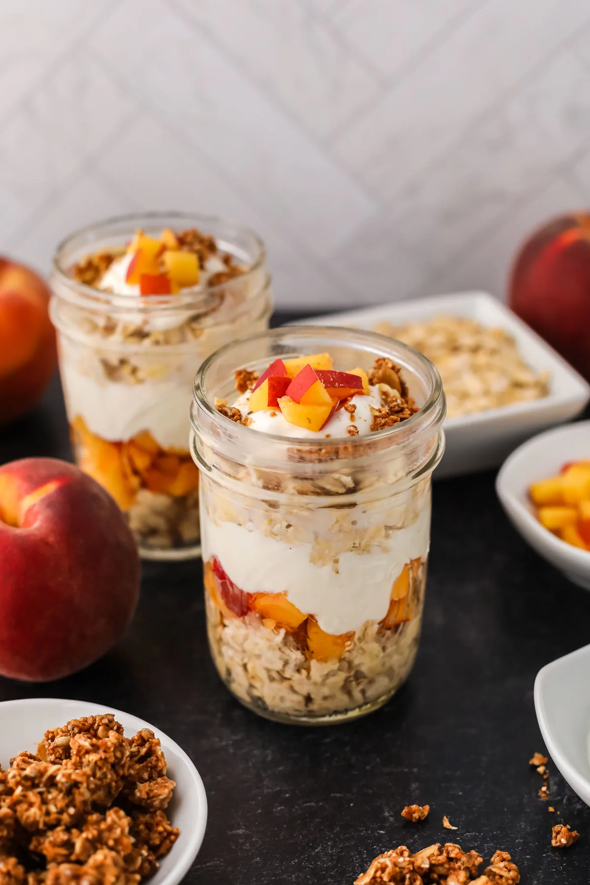 A picture of two containers of peach overnight oats with peaches in the background.