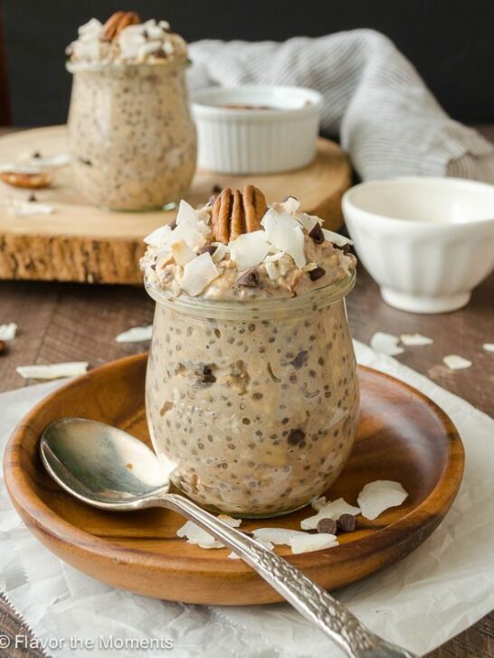 A cup of overnight oats filled to the brim and topped with nuts and coconut flakes. 