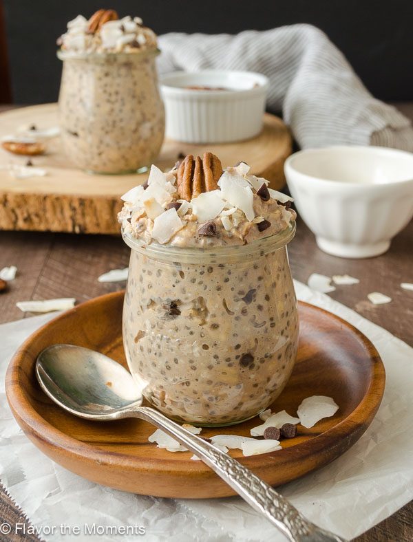 A cup of overnight oats filled to the brim and topped with nuts and coconut flakes.