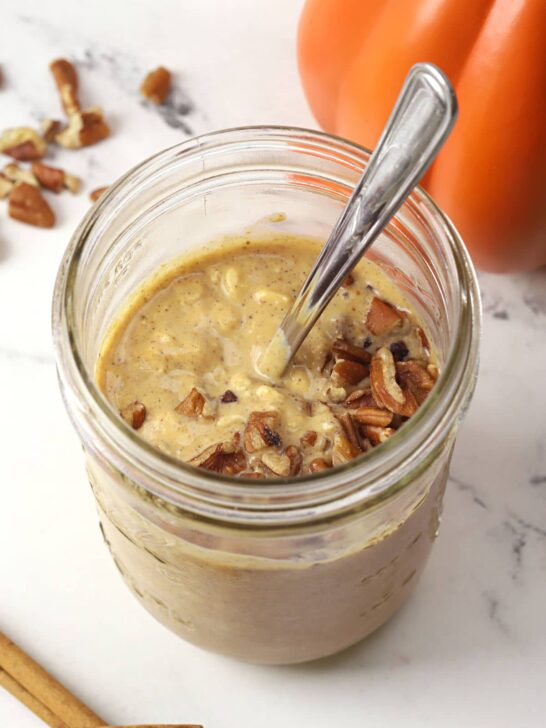 A jar of overnight oats topped with pecans and a pumpkin in the background. 