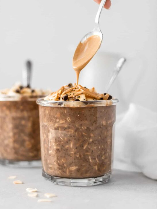 Two containers of chocolately overnight oats with a spoon of melted peanut butter pouring over the top. 