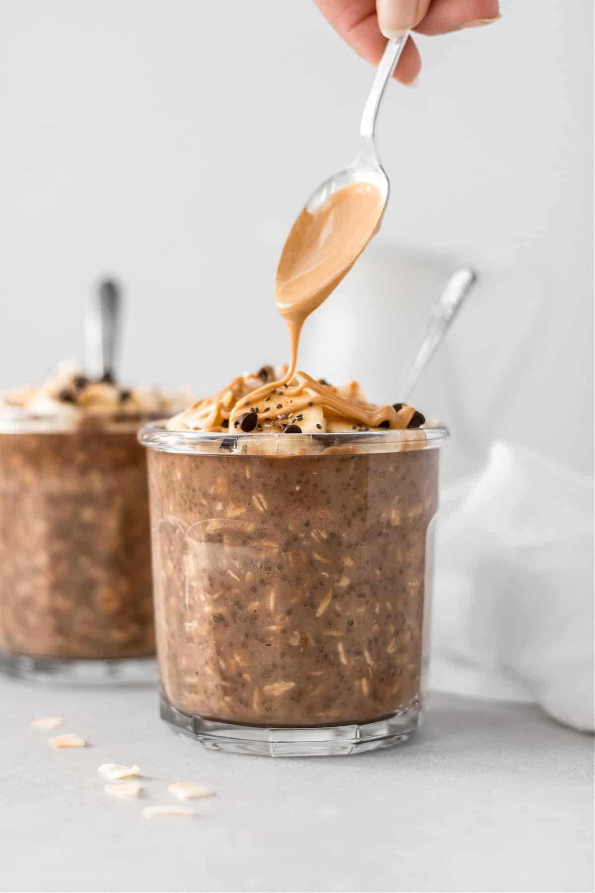 Two containers of chocolately overnight oats with a spoon of melted peanut butter pouring over the top.