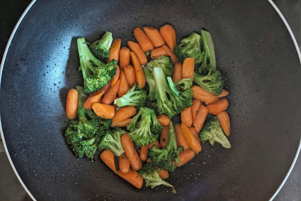 Carrots and broccoli cooking in a wok.