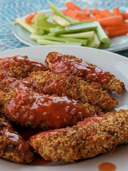 Air Fryer Buffalo Chicken tenders on a plate with vegetables in the background.