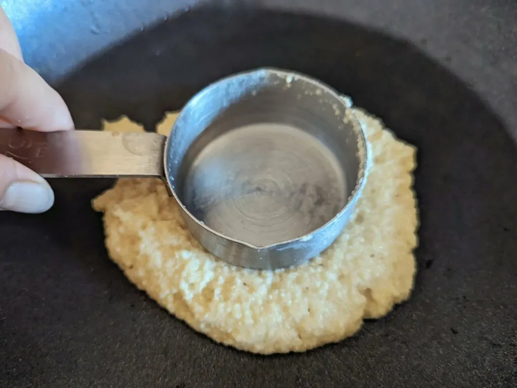 Some of the batter on a frying pan and tapped with a measuring cup. 