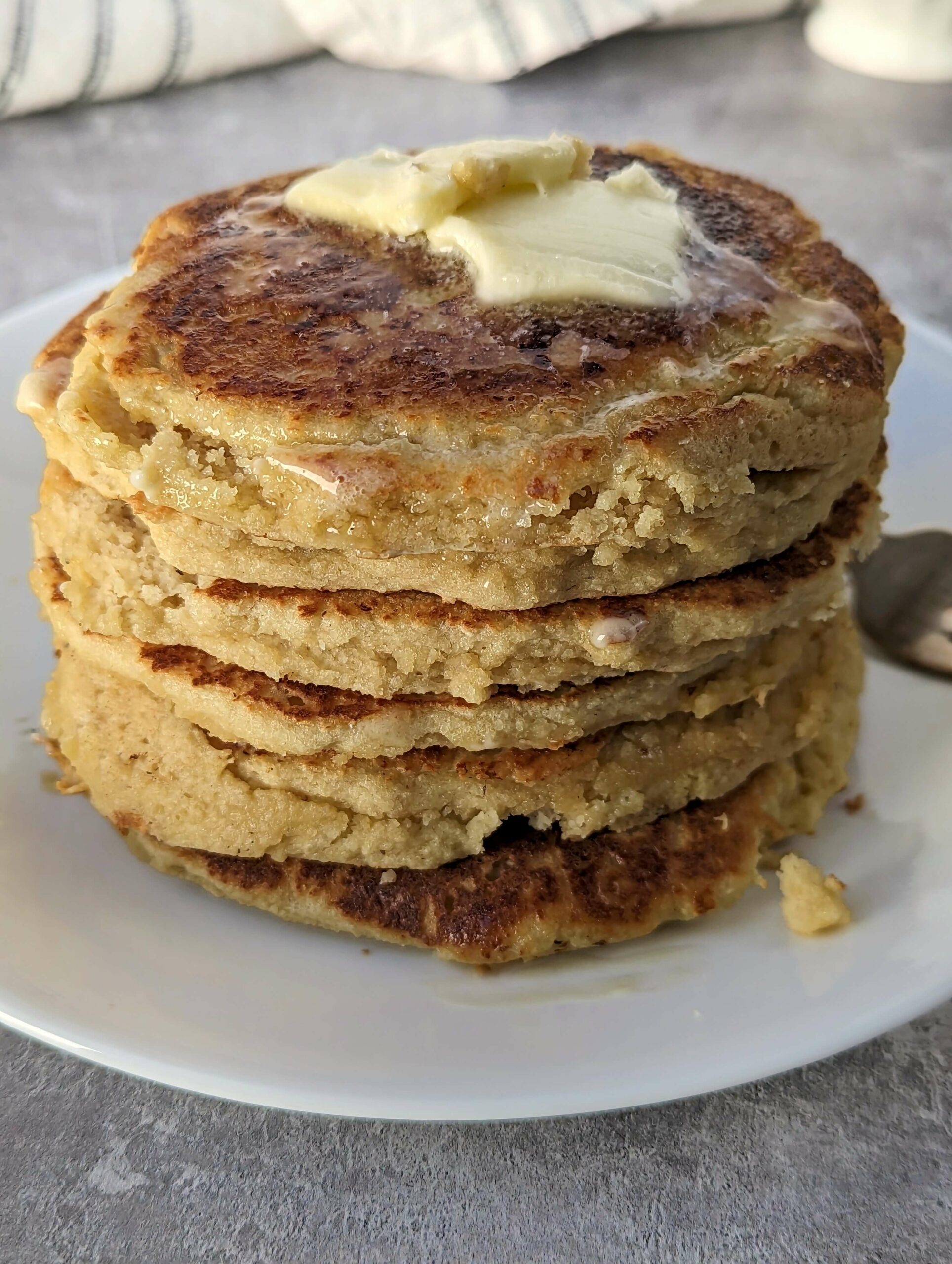 A close up of a stack of oat milk pancakes topped with melting butter and syrup. 