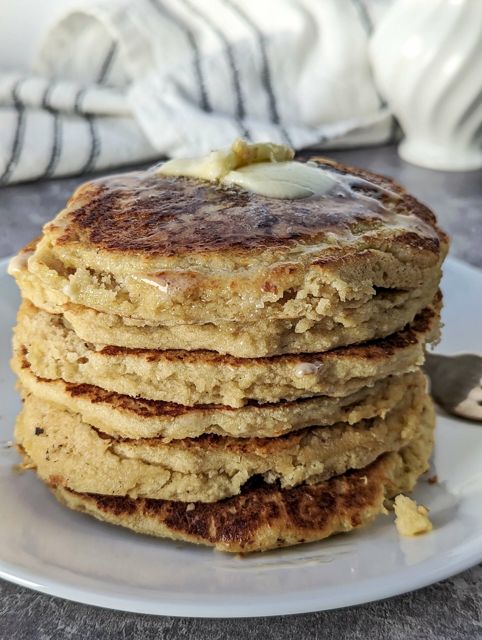 A close up of a stack of oat milk pancakes topped with butter and syrup. 