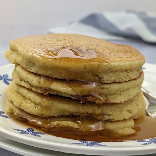 Pancakes stacked on a plate with syrup running down them.