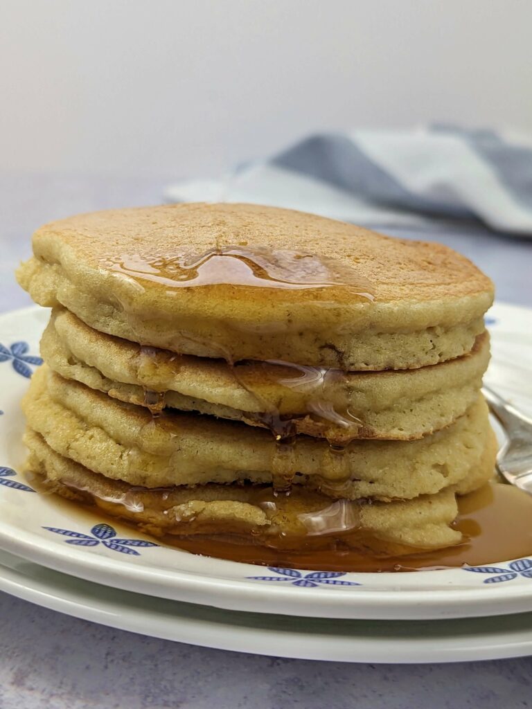 Pancakes stacked on a plate with syrup running down them.