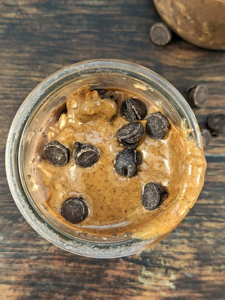 A over the top view of a glass jar full of protein overnight oats topped with melted peanut butter and chocolate chips. 