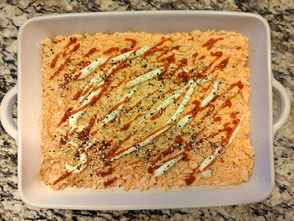 Rice and salmon in a baking dish and topped with mayonnaise and Sriracha.